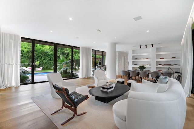 living area featuring a wall of windows, built in shelves, recessed lighting, and light wood-type flooring