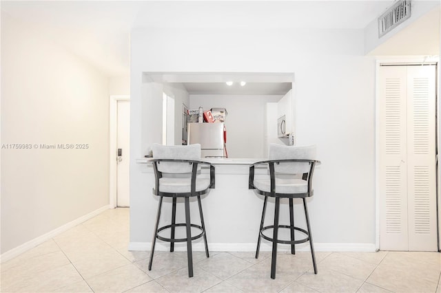 kitchen with visible vents, stainless steel microwave, a breakfast bar, light tile patterned floors, and freestanding refrigerator