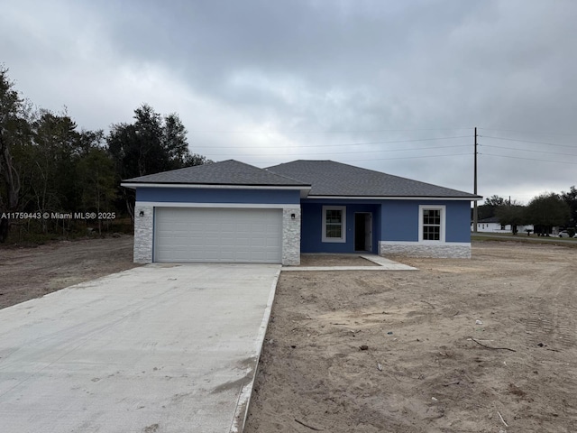 view of front of house featuring roof with shingles, stucco siding, a garage, stone siding, and driveway