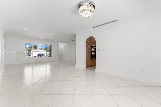 empty room featuring visible vents, light tile patterned floors, recessed lighting, an inviting chandelier, and arched walkways