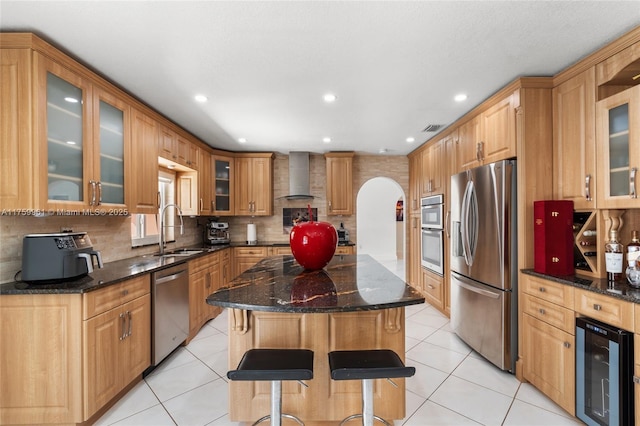 kitchen with a sink, wine cooler, arched walkways, appliances with stainless steel finishes, and wall chimney range hood