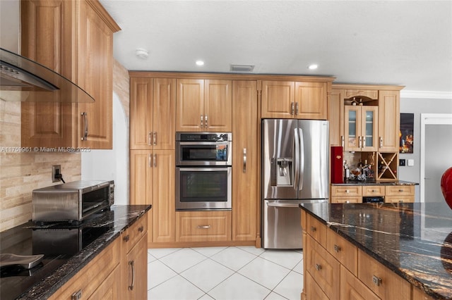 kitchen with visible vents, appliances with stainless steel finishes, light tile patterned flooring, wall chimney range hood, and glass insert cabinets