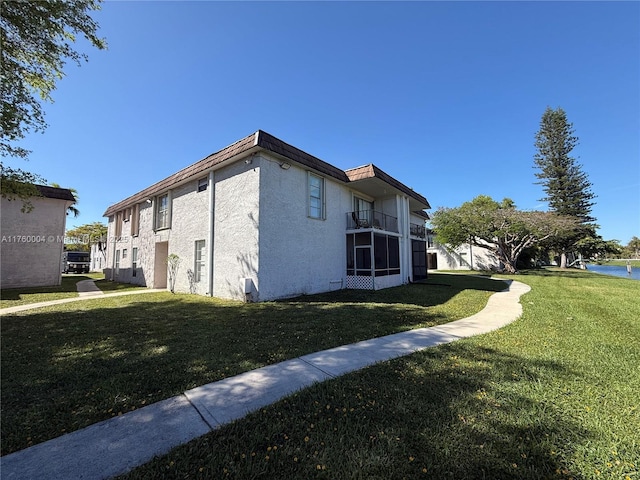 view of side of home featuring mansard roof, a lawn, and stucco siding