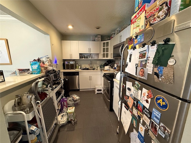 kitchen featuring dark tile patterned flooring, a sink, stainless steel appliances, light countertops, and white cabinetry