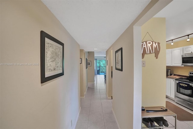 corridor with track lighting, light tile patterned floors, and baseboards