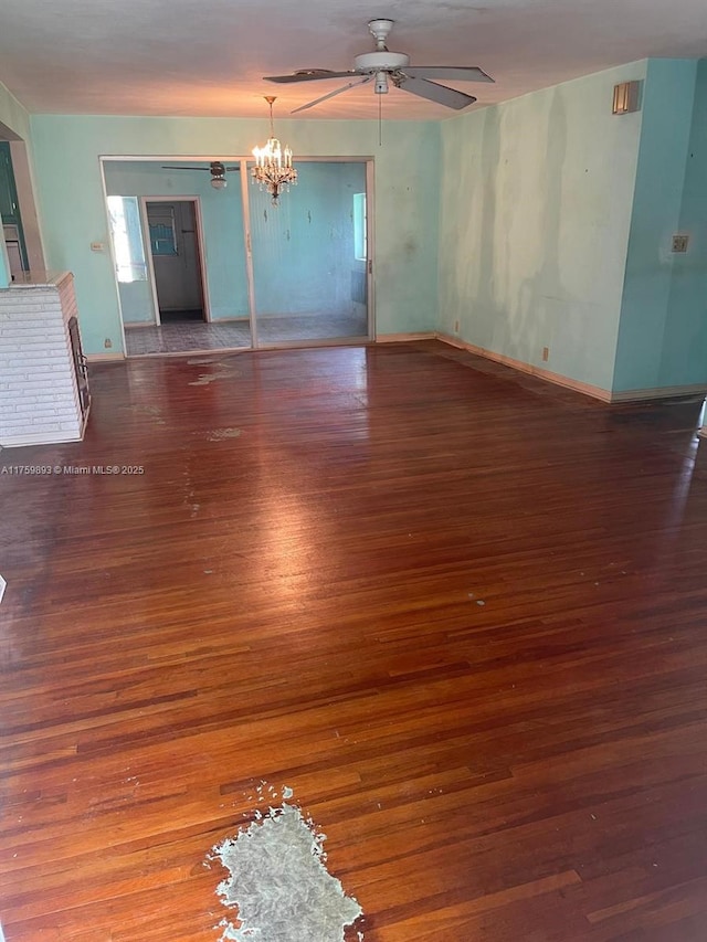 unfurnished living room with ceiling fan with notable chandelier, baseboards, and wood finished floors