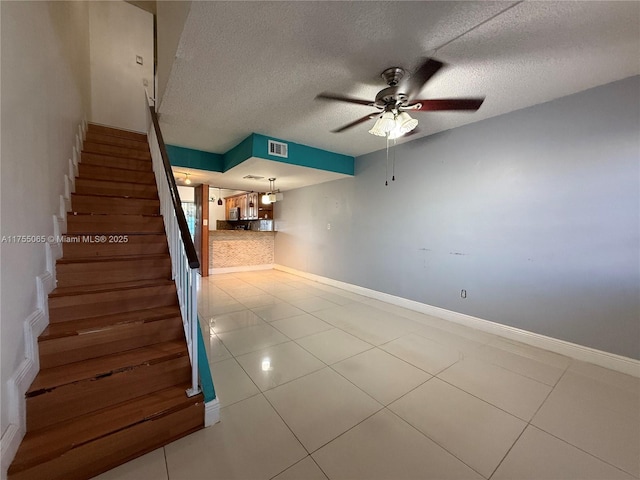 stairway with tile patterned floors, visible vents, a textured ceiling, baseboards, and ceiling fan