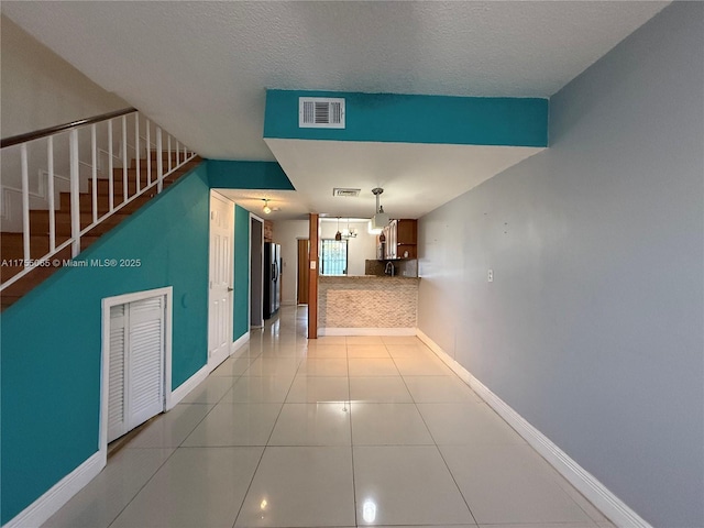 hallway with tile patterned floors, visible vents, stairway, and baseboards