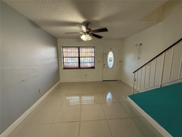 tiled foyer featuring a textured ceiling, stairway, baseboards, and ceiling fan