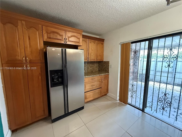 kitchen with backsplash, light tile patterned floors, brown cabinets, stainless steel refrigerator with ice dispenser, and a textured ceiling