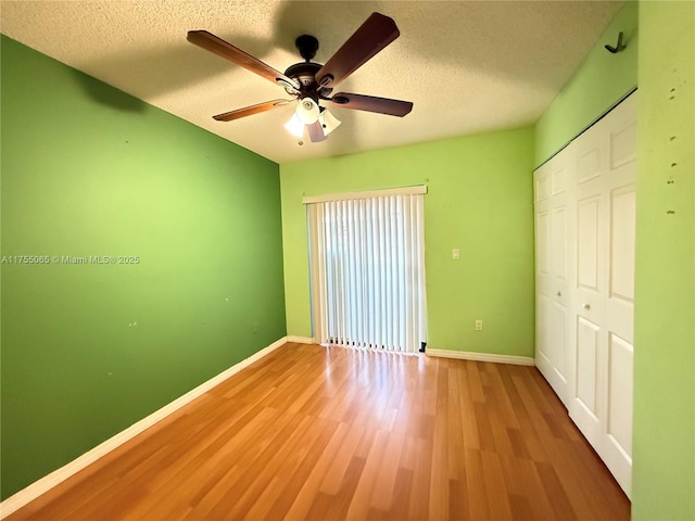 unfurnished bedroom with a closet, a textured ceiling, baseboards, and wood finished floors