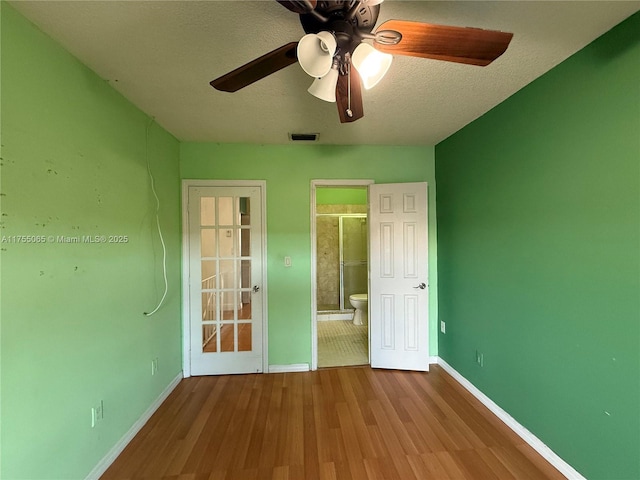 unfurnished bedroom featuring visible vents, ensuite bathroom, a textured ceiling, wood finished floors, and baseboards