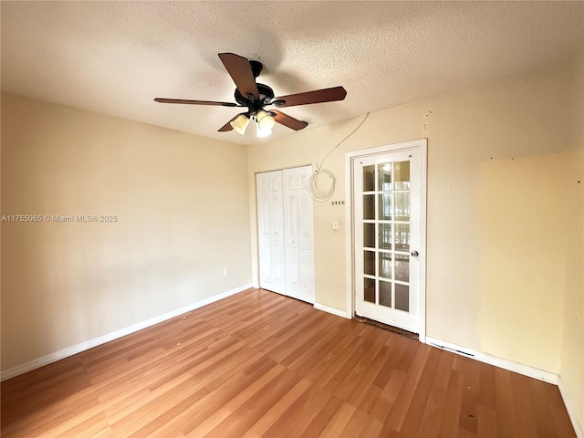 empty room with a textured ceiling, a ceiling fan, baseboards, and wood finished floors