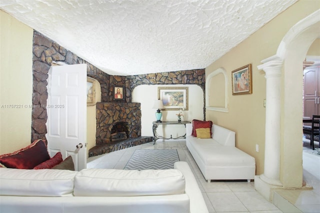 living area featuring a textured ceiling, arched walkways, a fireplace, light tile patterned floors, and ornate columns