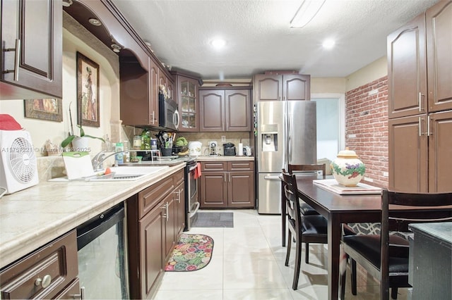 kitchen with a textured ceiling, tile countertops, stainless steel appliances, light tile patterned floors, and glass insert cabinets