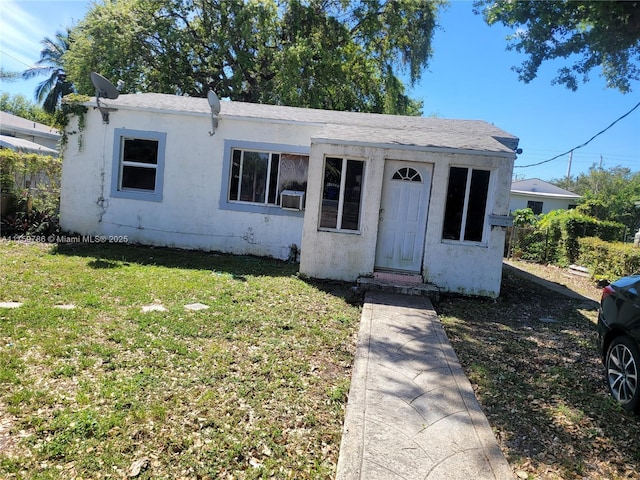 view of front of house with a shingled roof, a front yard, cooling unit, and stucco siding