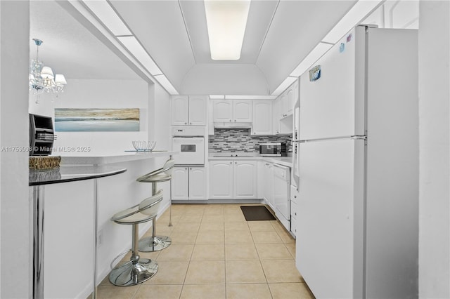 kitchen featuring backsplash, lofted ceiling, light tile patterned flooring, white appliances, and white cabinetry