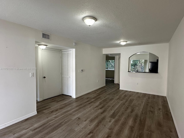 empty room with visible vents, arched walkways, baseboards, and dark wood finished floors