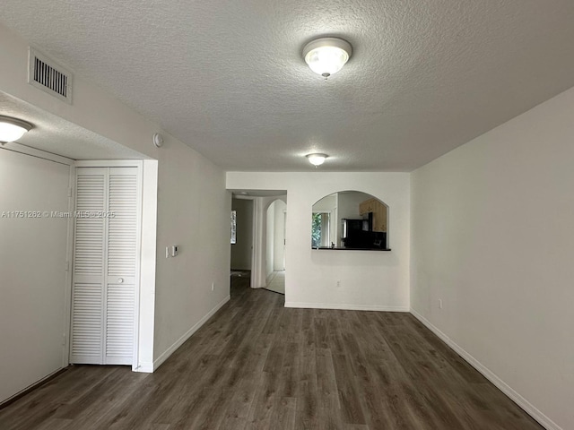 empty room featuring visible vents, dark wood-type flooring, baseboards, arched walkways, and a textured ceiling