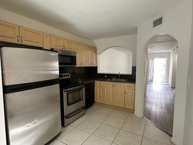 kitchen featuring visible vents, light brown cabinetry, a sink, dark countertops, and stainless steel appliances