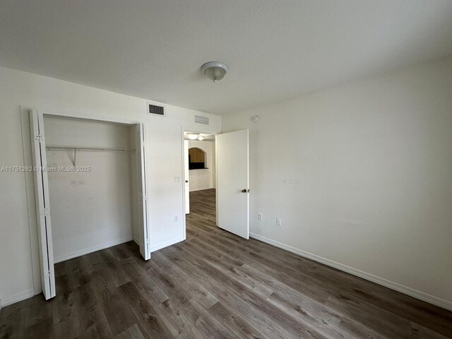 unfurnished bedroom with dark wood-style floors, visible vents, a closet, and baseboards