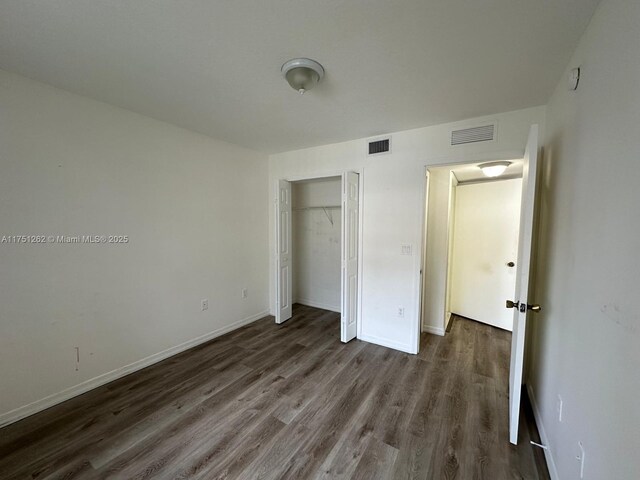 unfurnished bedroom featuring visible vents, baseboards, dark wood-type flooring, and a closet