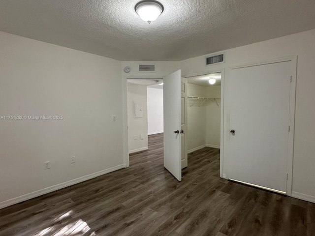 unfurnished bedroom featuring dark wood finished floors, visible vents, a textured ceiling, and a closet