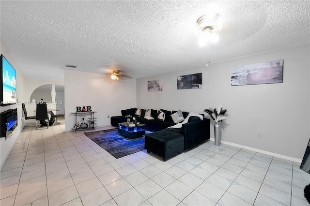 living room with visible vents, baseboards, light tile patterned floors, arched walkways, and a textured ceiling