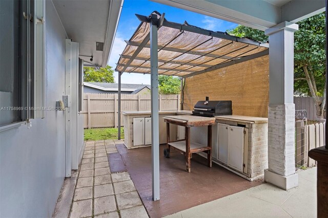 view of patio featuring an outdoor kitchen, a grill, a pergola, and fence