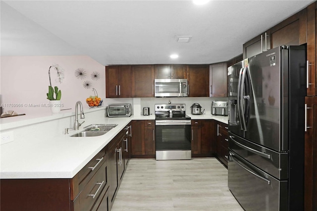 kitchen with a sink, stainless steel appliances, light countertops, dark brown cabinetry, and light wood-type flooring