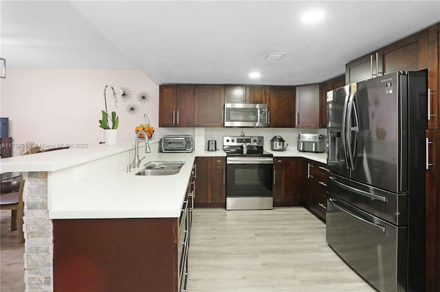 kitchen with light wood finished floors, a peninsula, a sink, light countertops, and appliances with stainless steel finishes