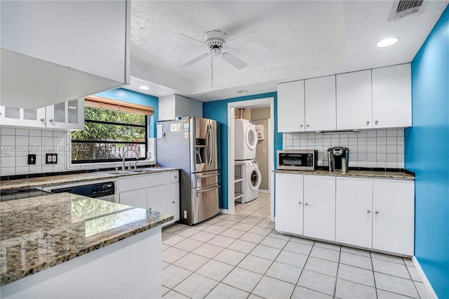 kitchen featuring light stone countertops, visible vents, a sink, stainless steel appliances, and stacked washer / drying machine