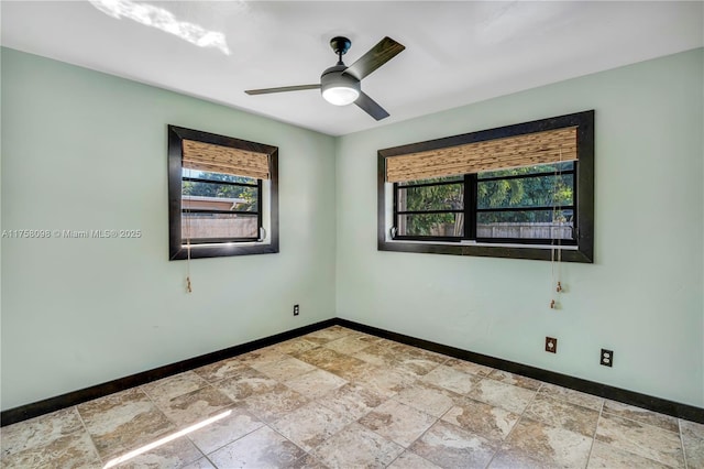 unfurnished room with stone finish floor, a ceiling fan, and baseboards