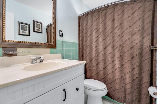 full bath featuring a shower with curtain, toilet, tile walls, wainscoting, and vanity