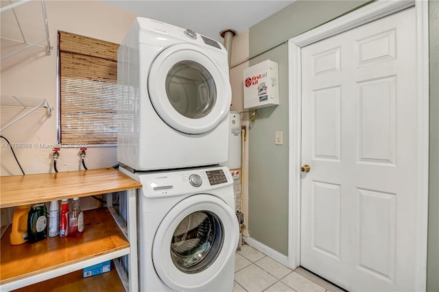 laundry room featuring light tile patterned flooring, laundry area, stacked washer / drying machine, and baseboards