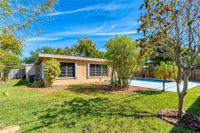 rear view of house featuring cooling unit, a lawn, a fenced backyard, and stucco siding