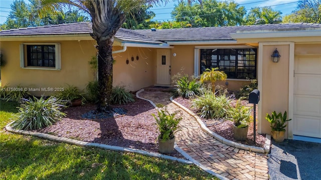 view of exterior entry with a tile roof, an attached garage, and stucco siding