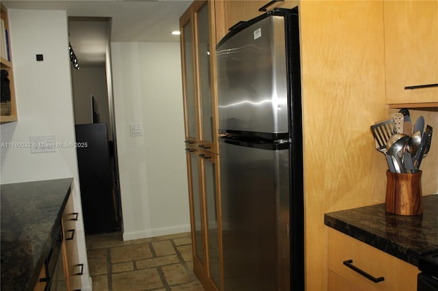 kitchen with dark countertops, refrigerator, stone tile floors, freestanding refrigerator, and glass insert cabinets