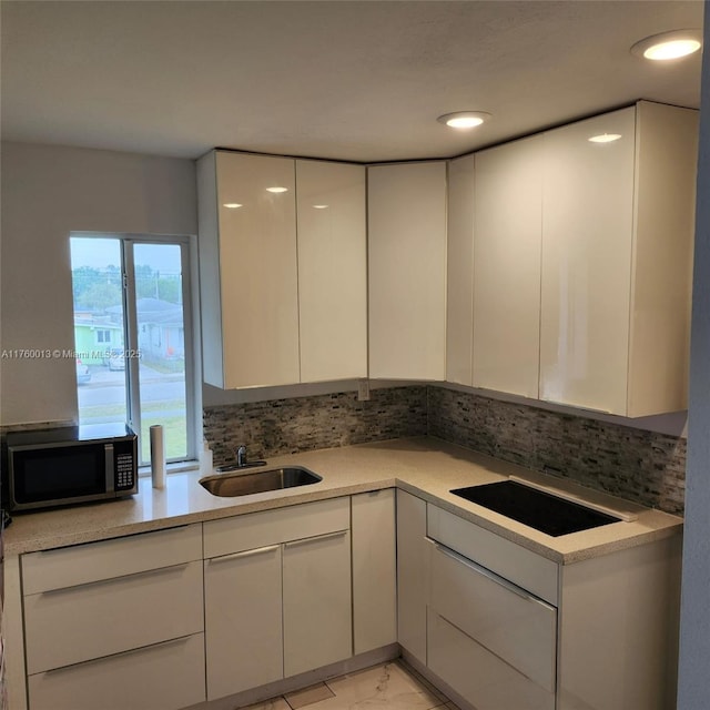 kitchen with tasteful backsplash, stainless steel microwave, white cabinets, and a sink