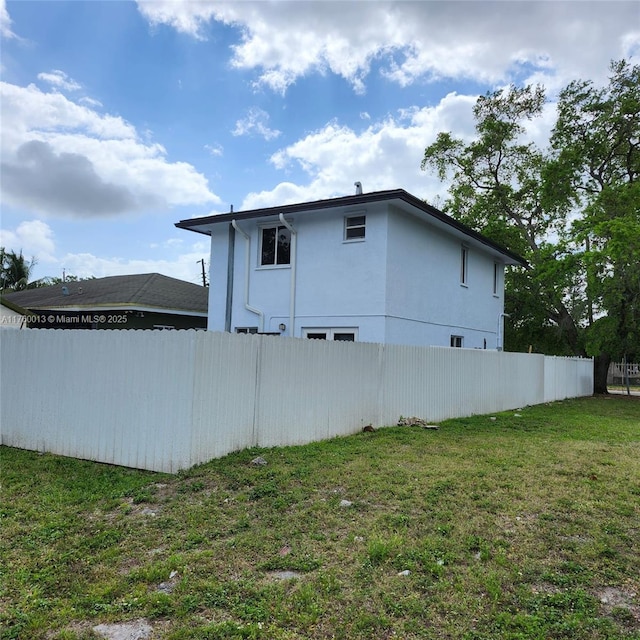 view of home's exterior with fence, a lawn, and stucco siding