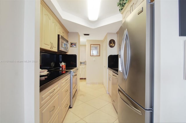 kitchen featuring dark countertops, visible vents, light tile patterned flooring, stainless steel appliances, and a raised ceiling