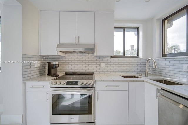 kitchen with backsplash, light stone countertops, under cabinet range hood, stainless steel appliances, and white cabinetry