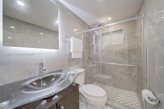 bathroom with tile walls, a stall shower, toilet, and vanity