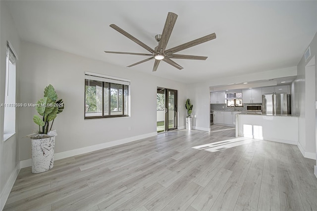 unfurnished living room with visible vents, a sink, light wood finished floors, baseboards, and ceiling fan