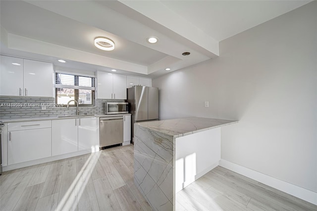 kitchen with tasteful backsplash, a tray ceiling, a peninsula, stainless steel appliances, and a sink