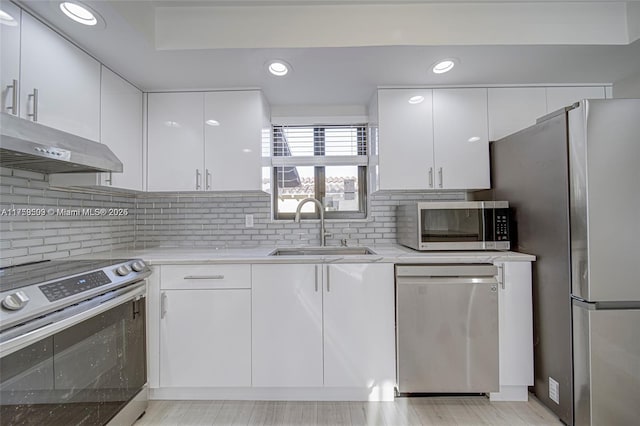 kitchen featuring tasteful backsplash, under cabinet range hood, appliances with stainless steel finishes, white cabinetry, and a sink