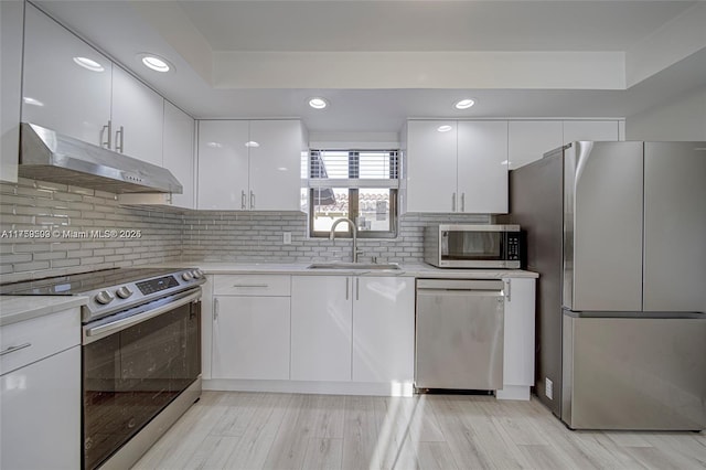 kitchen featuring a sink, light countertops, white cabinets, under cabinet range hood, and appliances with stainless steel finishes