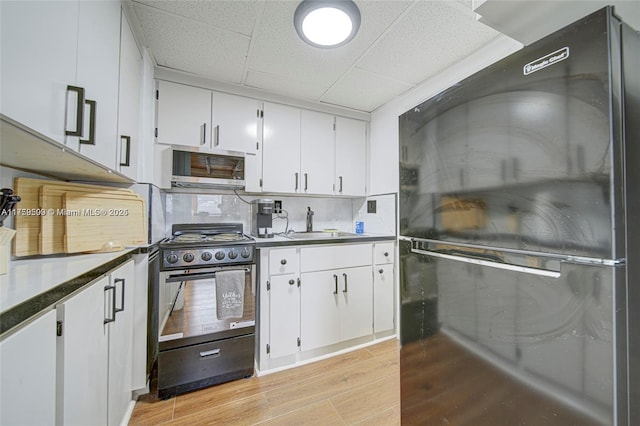 kitchen with gas stove, light wood-style flooring, white cabinets, a paneled ceiling, and stainless steel microwave