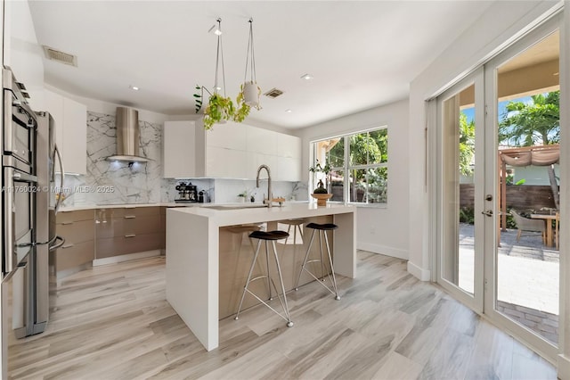 kitchen with visible vents, a sink, a kitchen breakfast bar, wall chimney exhaust hood, and modern cabinets