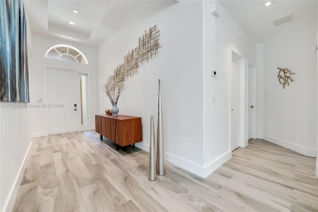 entryway with light wood-style flooring, a raised ceiling, baseboards, and a towering ceiling